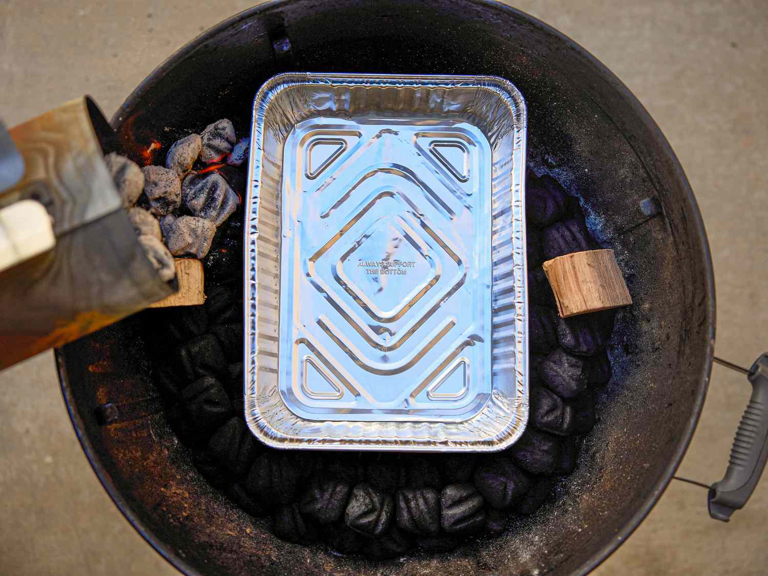 Setup of a smoker for cooking with an aluminum drip pan charcoal and wood pieces