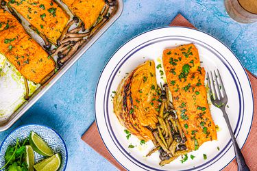 A plated salmon dish alongside a sheet pan with prepared salmon and vegetables, garnished and ready to serve