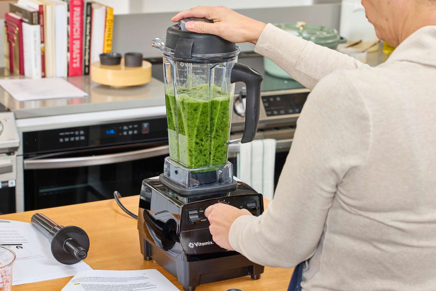 A person using the Vitamix 5200 Professional-Grade Blender on a counter to blend green items