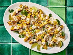 Bright colorful photo of grilled corn, topped with sauce, cheese cilantro and limes. 
