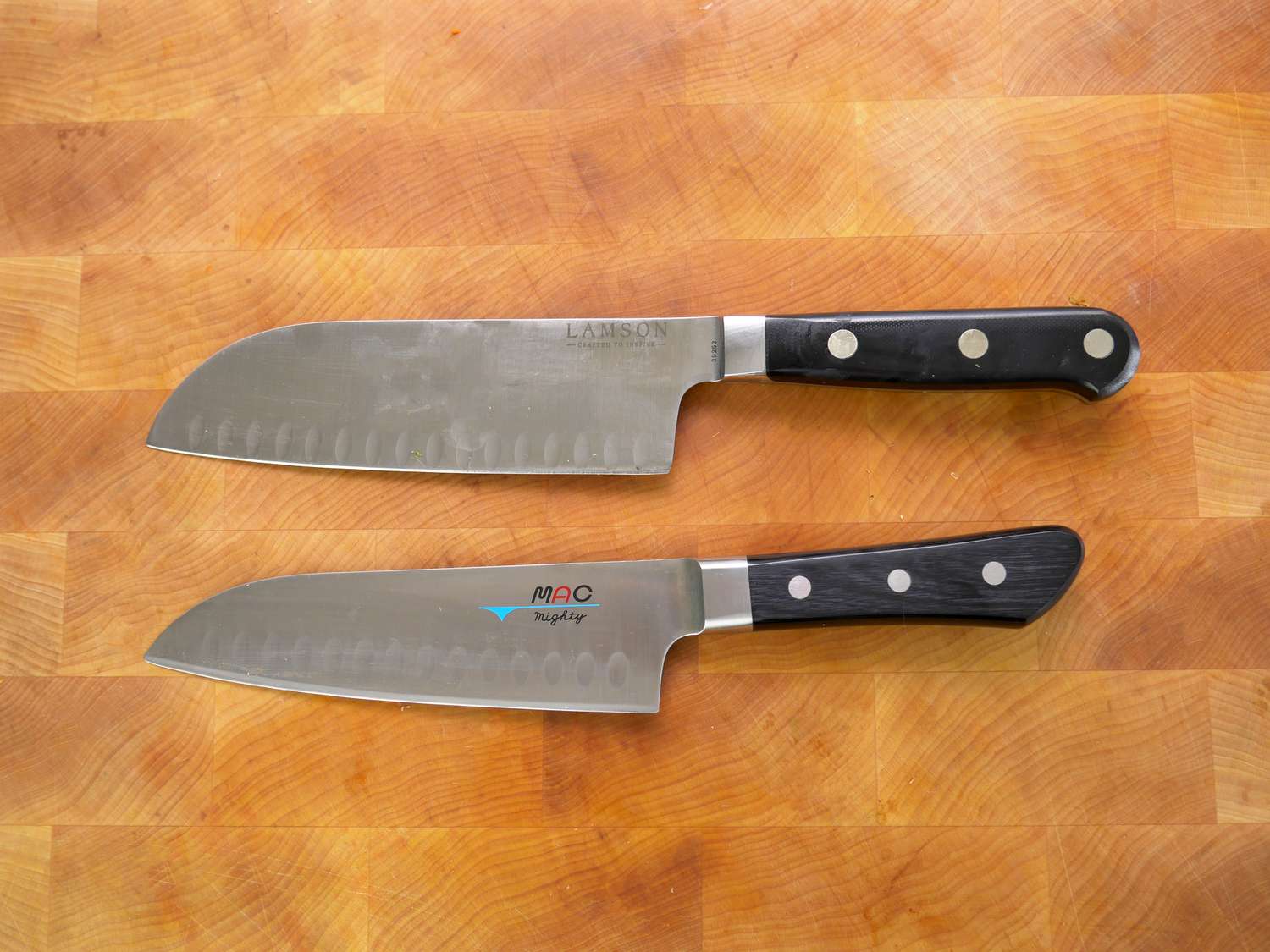 two santoku knives, one with a straight edge blade and one with a curved blade, on a cutting board