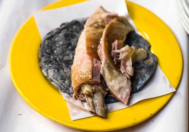 Lamb barbacoa on a blue corn tortilla on a yellow plate.