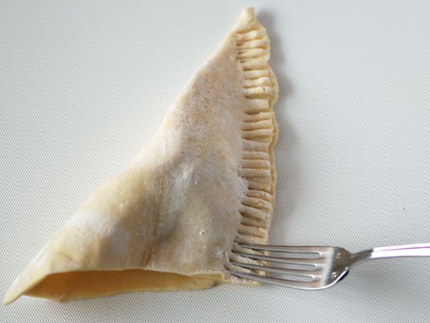 The square of puff pastry has been folded over the filling and crimped with a fork.