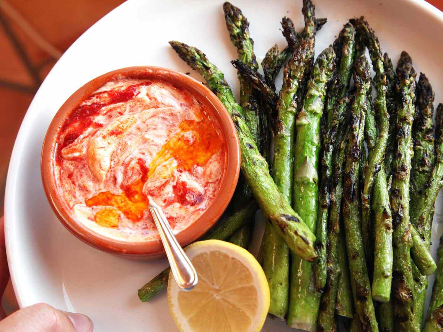 Grilled asparagus on a plate with harissa aioli and lemon.