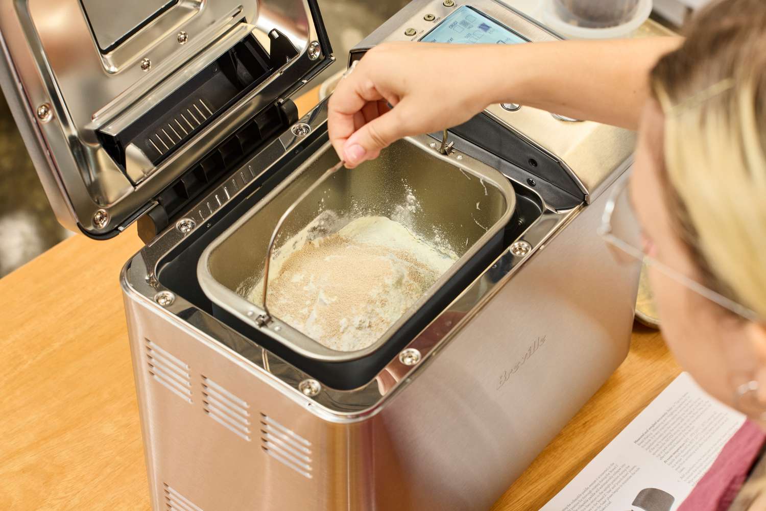 A person placing a basket filled with dough inside of the Breville Custom Loaf Bread Maker