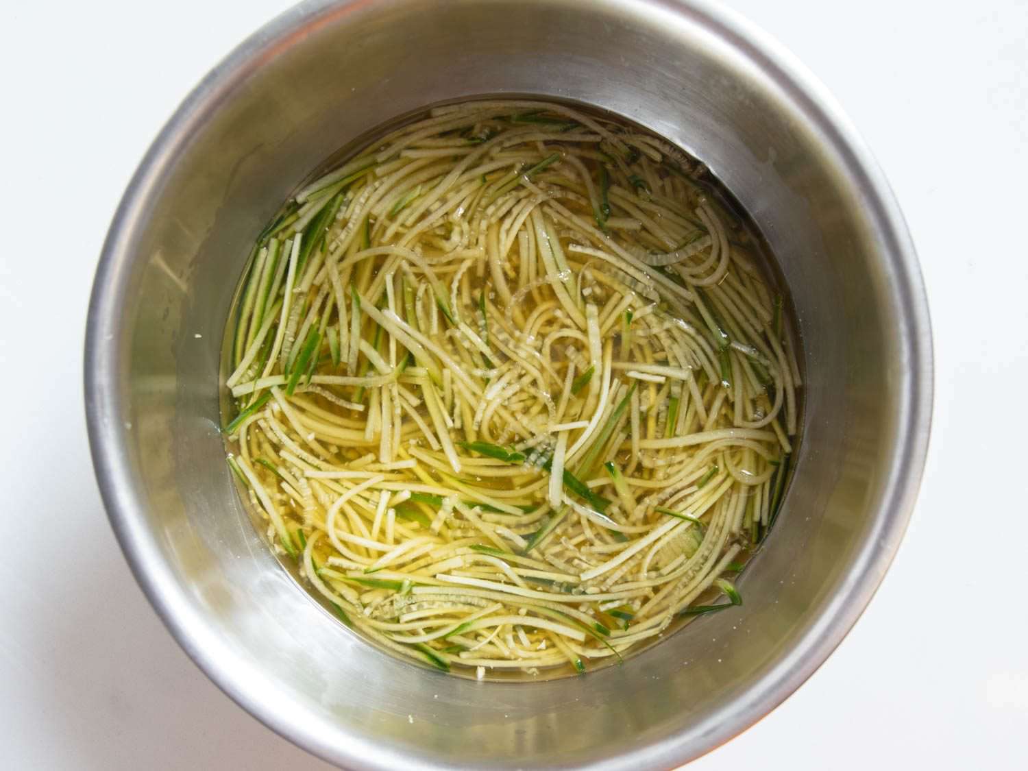 Oi naengguk, a chilled Korean cucumber soup, still in the mixing bowl before ice has been added to the thin strands of cucumber and lightly seasoned broth.