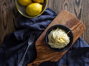 A bowl of pasta al limone on an olive wood cutting board with a dark blue linen napkin.