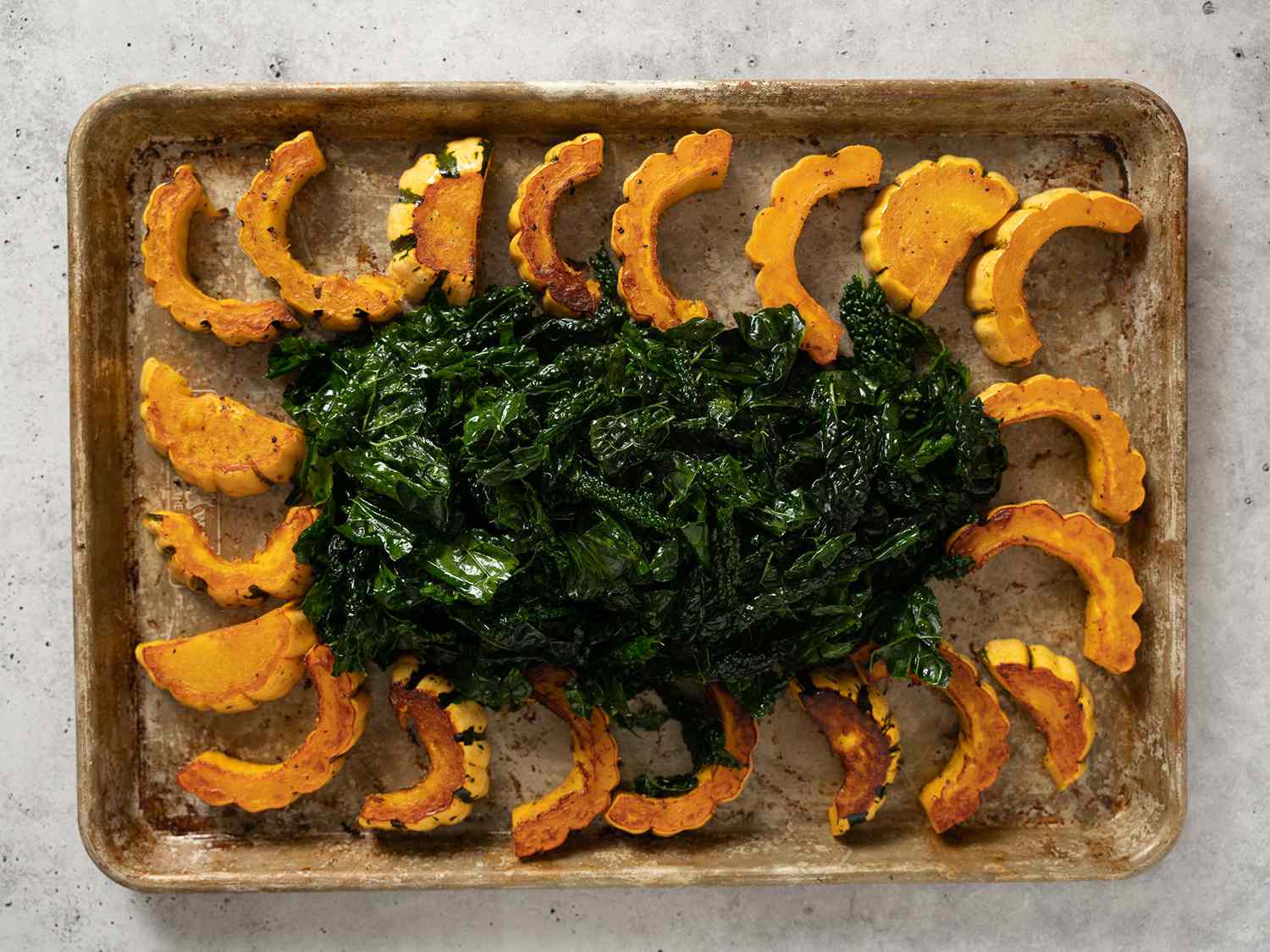 Squash and kale on a rimmed baking sheet with kale in the center.