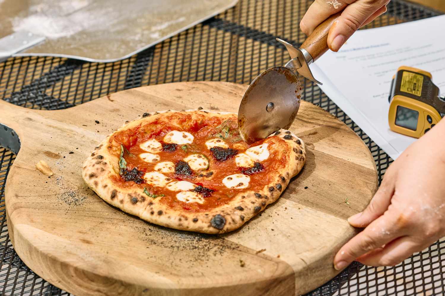 A person cuts a pizza cooked in the Ooni Karu 2 Multi-Fuel Pizza Oven