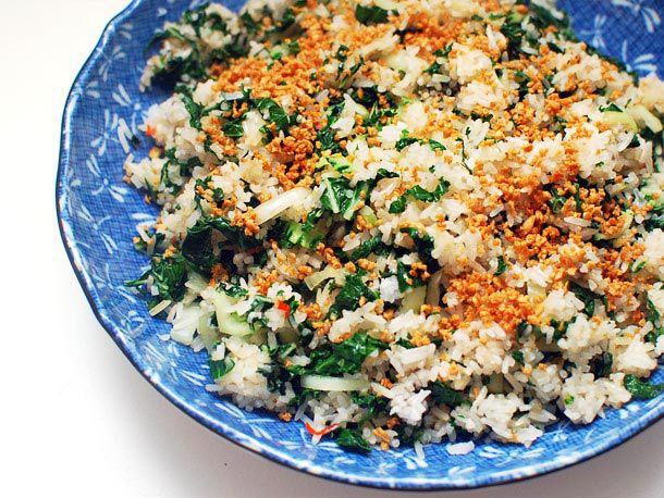 A plate of fried rice with greens and a garnish of fried minced garlic.