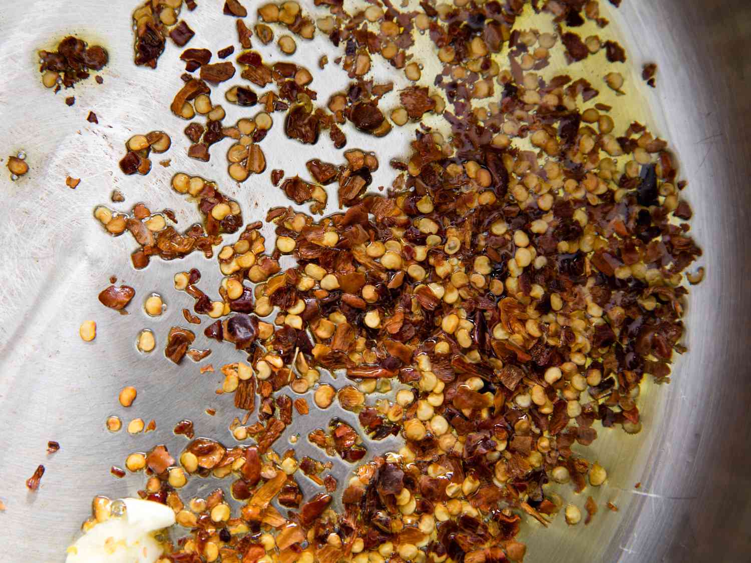 Overhead closeup of a skillet in which garlic and chile flakes are being cooked in olive oil.