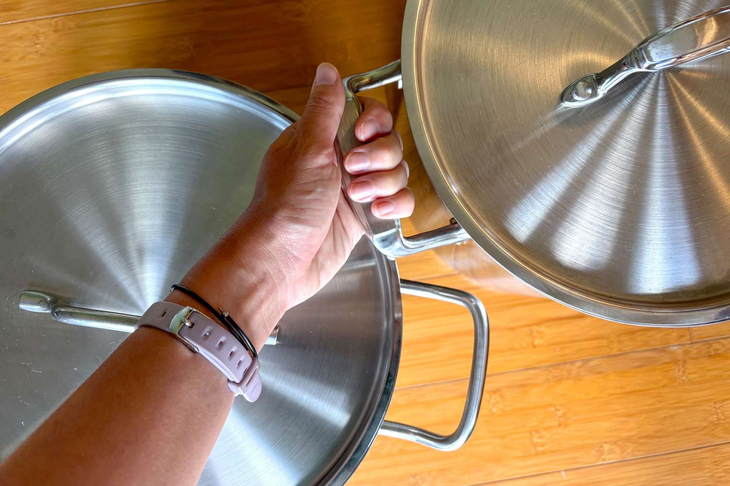 Two stockpots on a wooden countertop. A person is grabbing the handle of one of the stockpots.