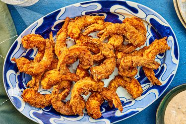 Southern Fried Shrimp on a blue printed plate, with dip, and sparkling water, and a blue textile. 