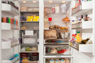 An open refrigerator stocked with various groceries and food items on the shelves and compartments including beverages and produce