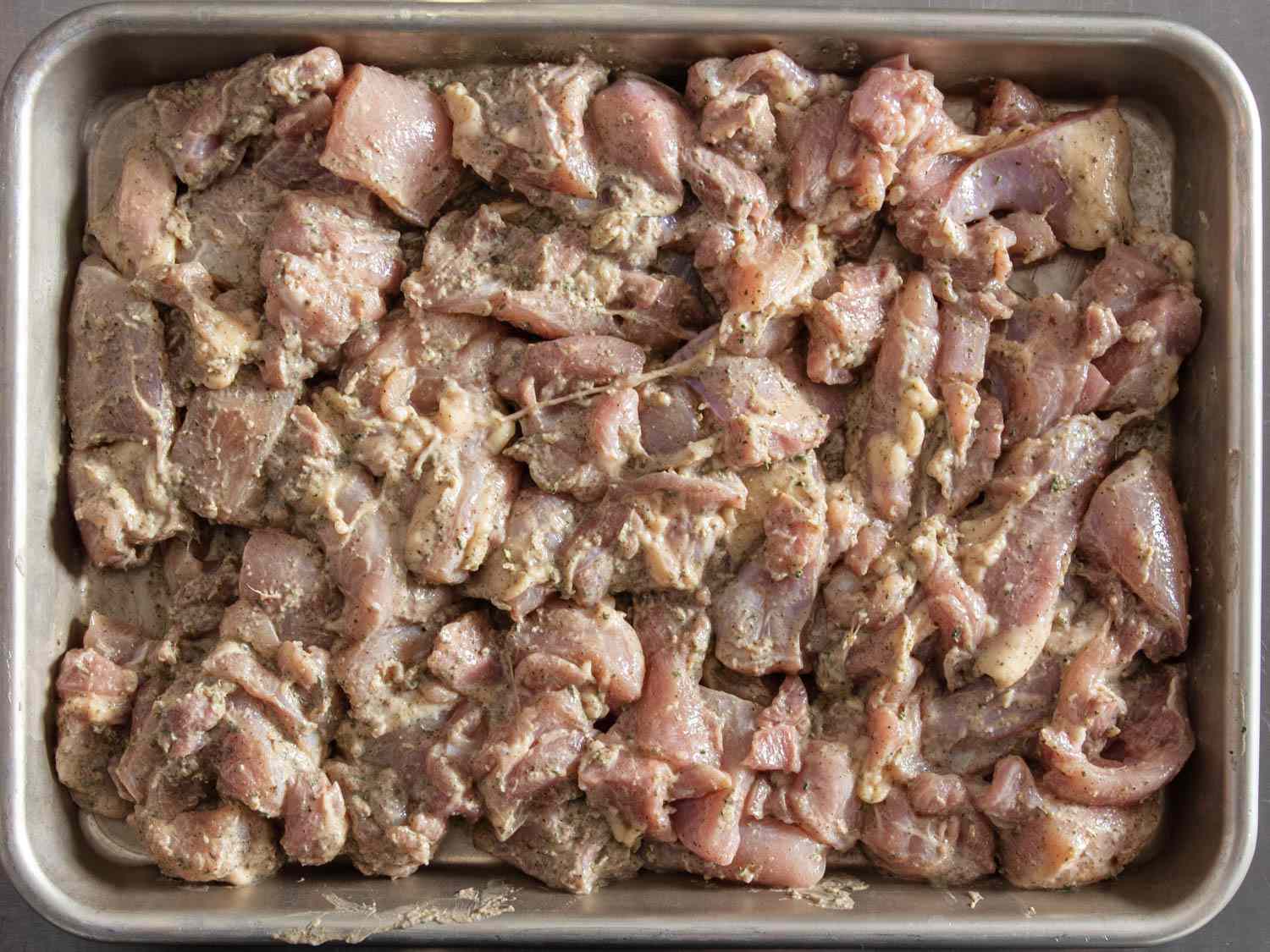 Overhead close-up of the marinade-coated chicken pieces arranged in an even layer in a quarter sheet pan.