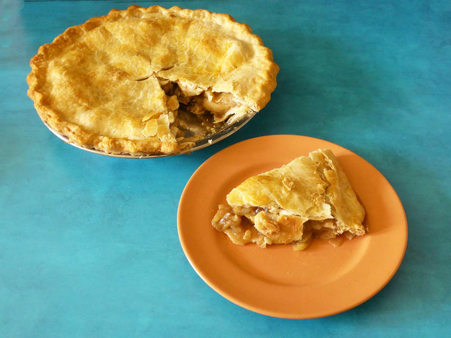 A slice of pie on a plate in front of the apple pie in the norpro pan.