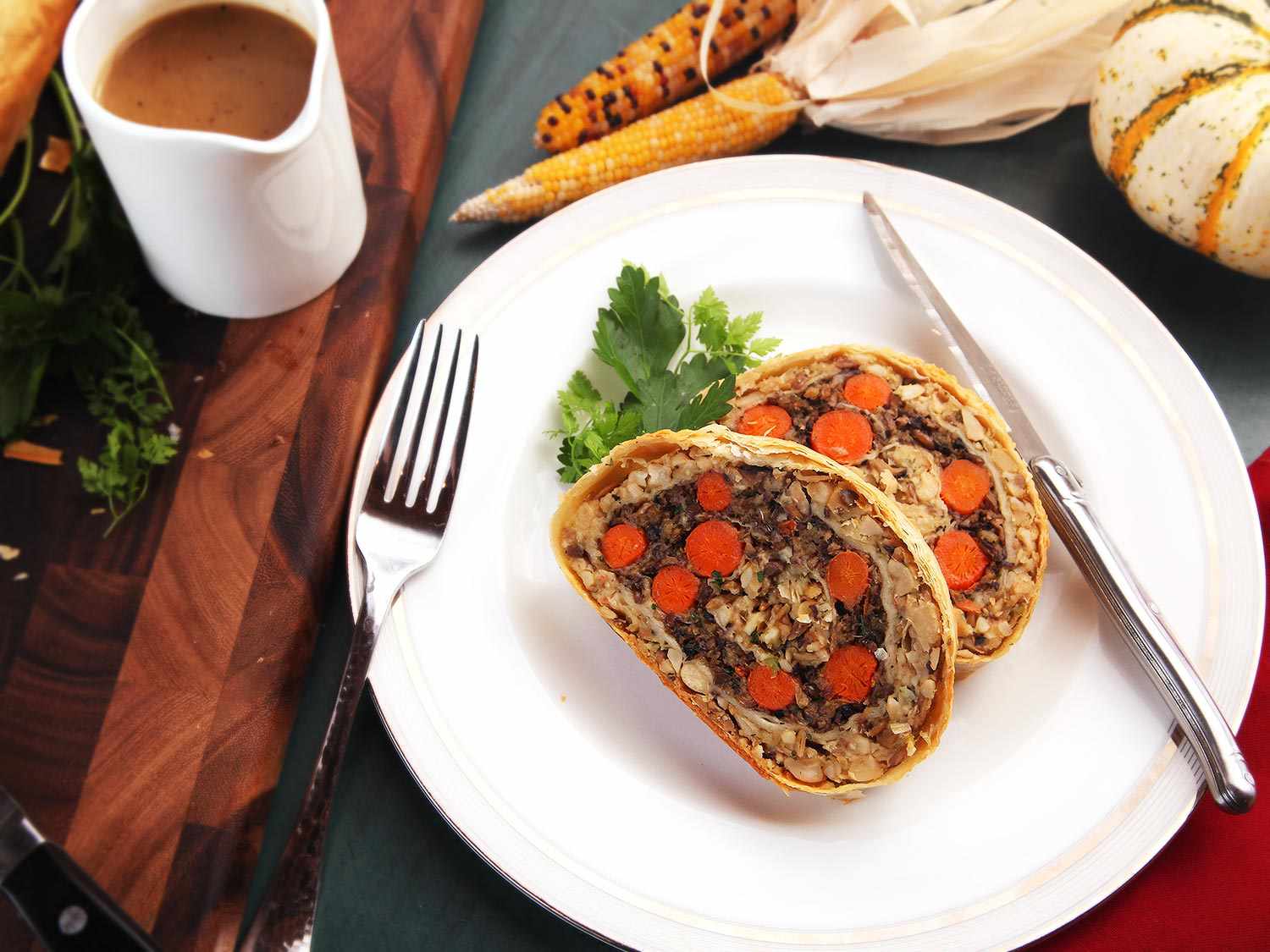 Vegetables Wellington slices resting on a plate with gravy boat and cutlery alongside.