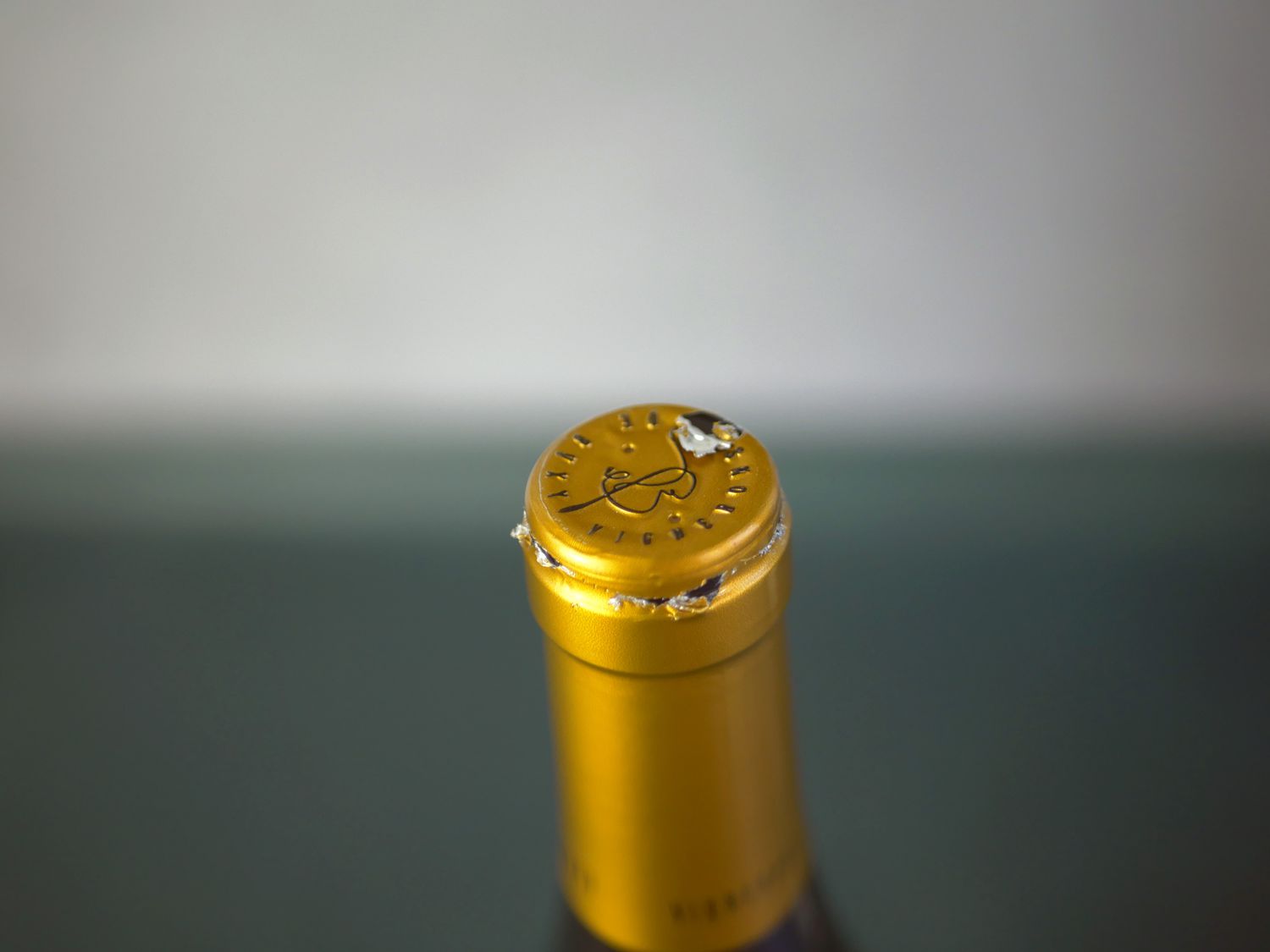 a closeup shot of a bottle of wine with a foil cap that has been sliced but is rather frayed.