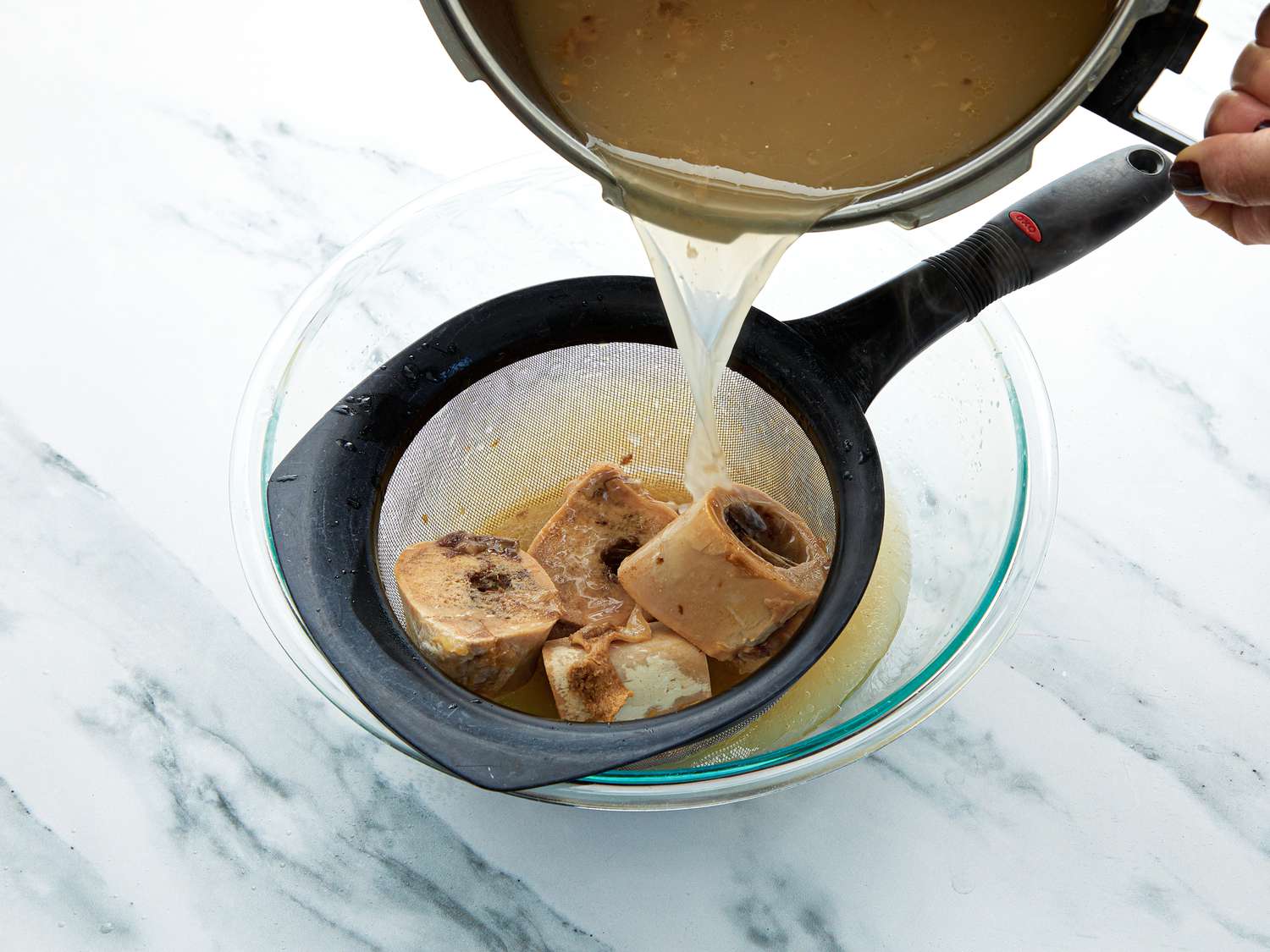 Straining bones and beef broth into a bowl