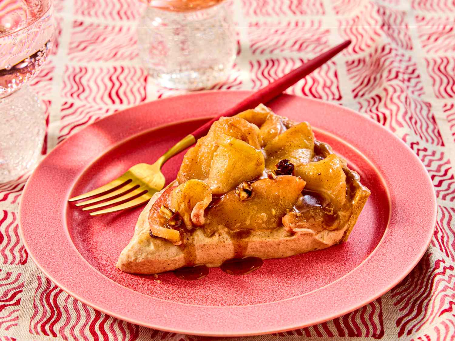 A slice of caramelized apple tart on a red plate garnished with chestnut cream and paired with a gold fork