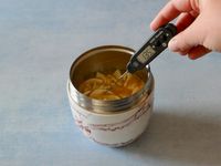 person taking temperature of soup in swell thermos