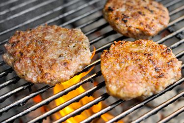 Three breakfast sausage patties cooking on a grill. 