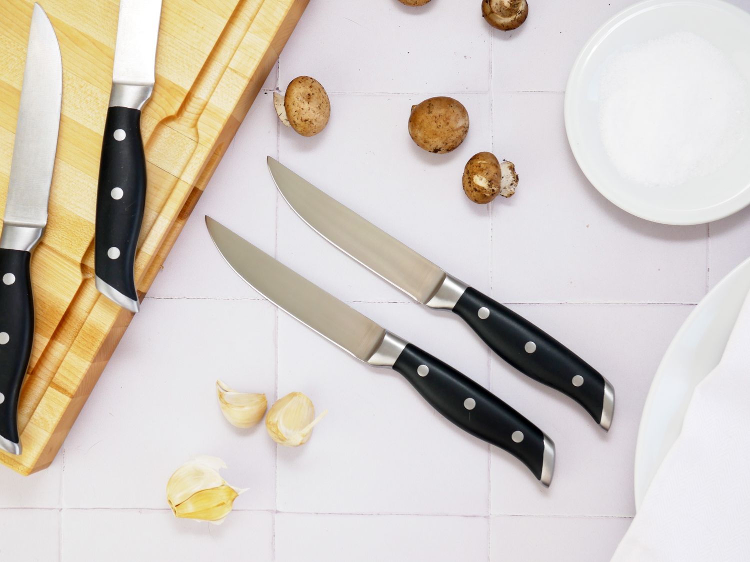 two quince steak knives on a white tile surface