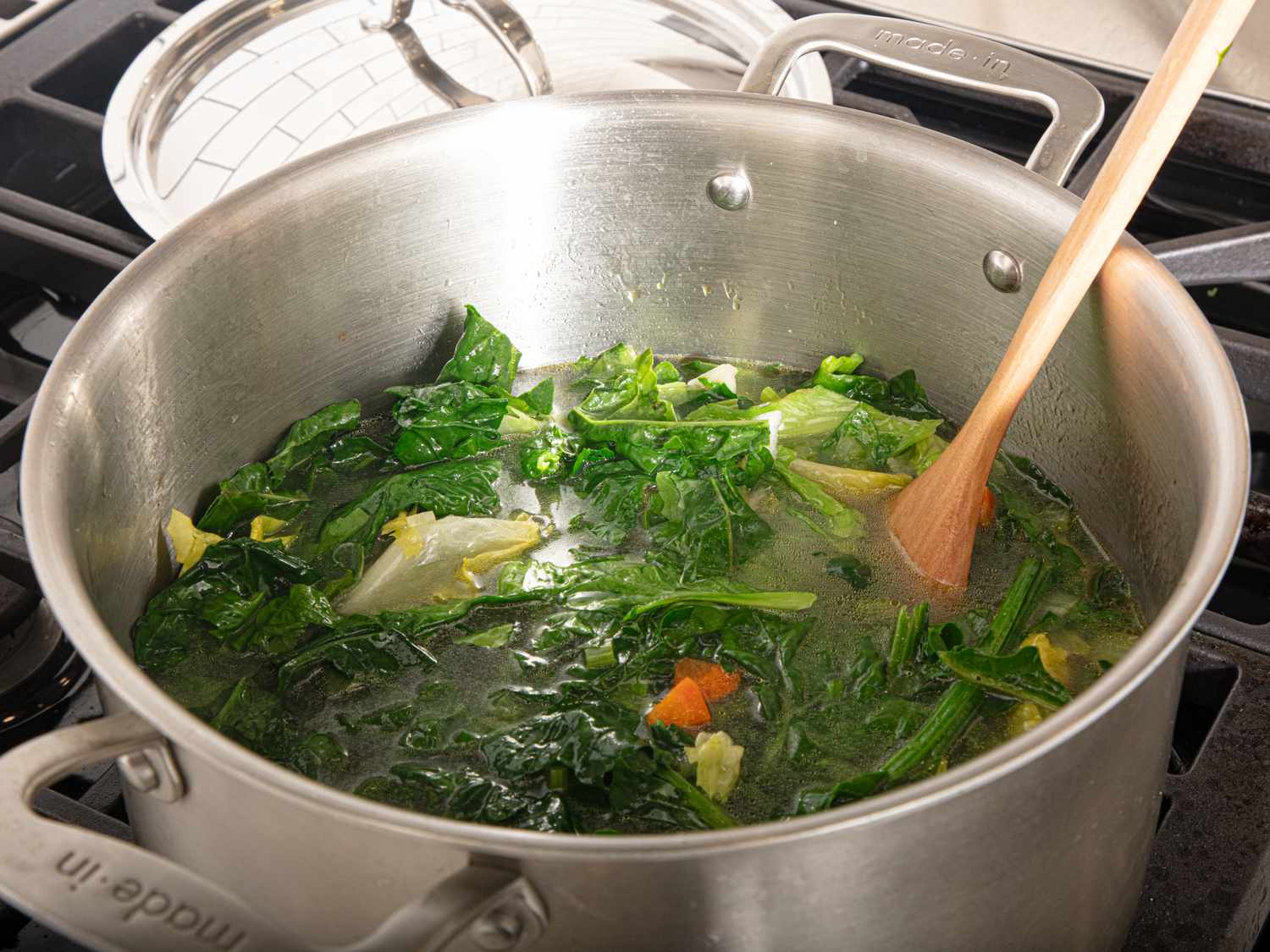 Soup being prepared in a pot featuring leafy greens and vegetables