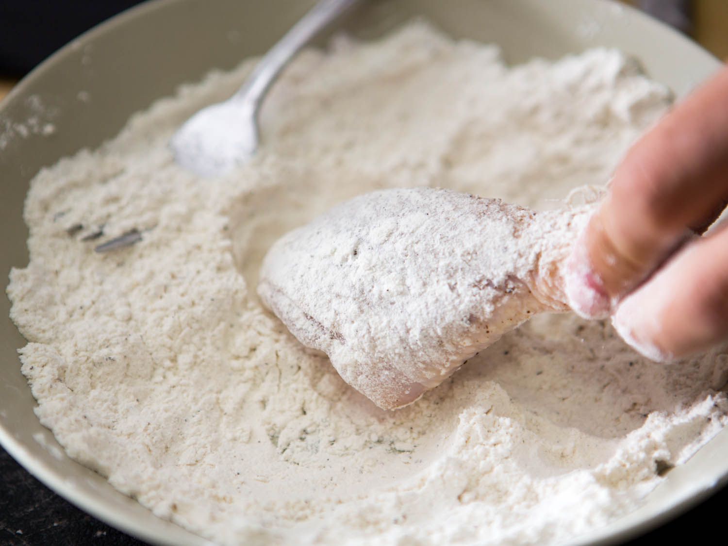 Dredging chicken pieces in seasoned flour for Maryland fried chicken.