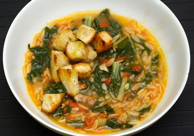 Overhead view of Swiss chard and pasta soup in a deep white bowl.