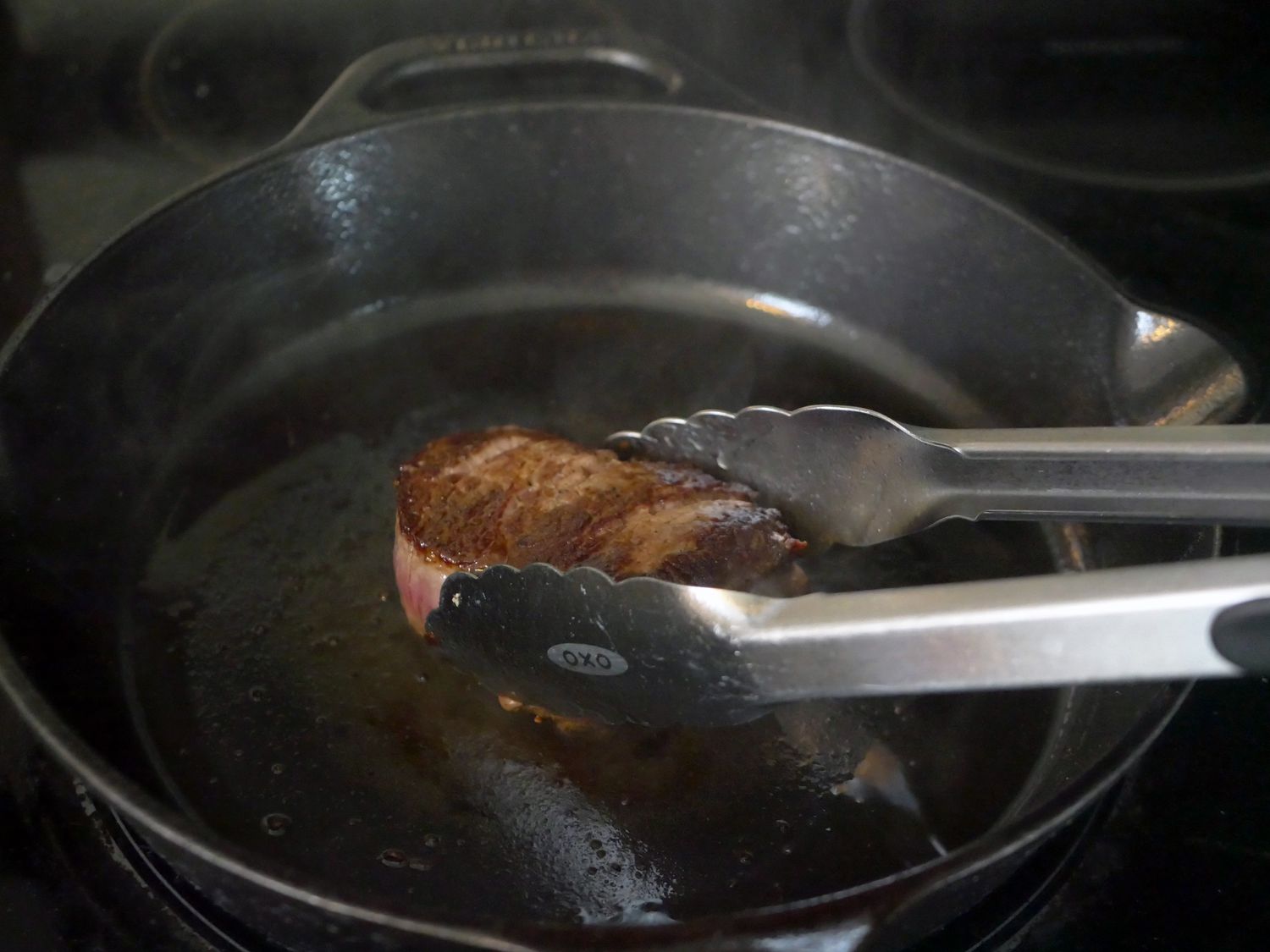 flipping a steak in a cast iron skillet