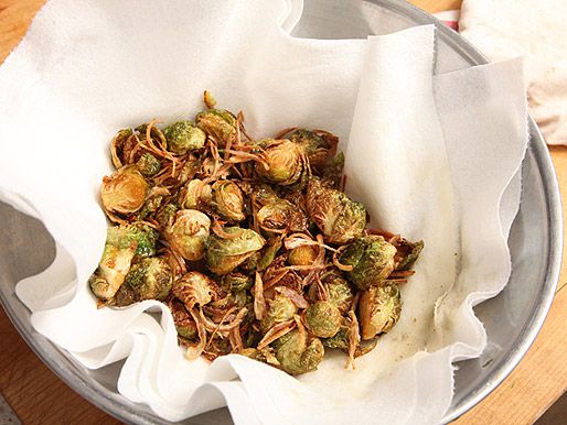 Already fried Brussels sprouts and shallots draining on a paper towel in a silver bowl.