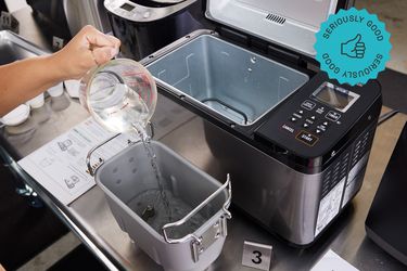 the zojirushi bread maker with someone putting water into the bread pan