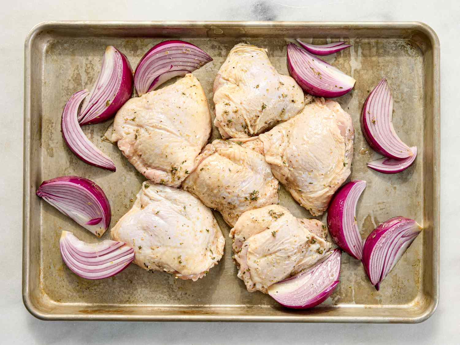 Raw seasoned chicken thighs and slices of red onion arranged on a baking sheet