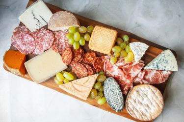 A charcuterie board with cheeses, sliced salami, and grapes on it.