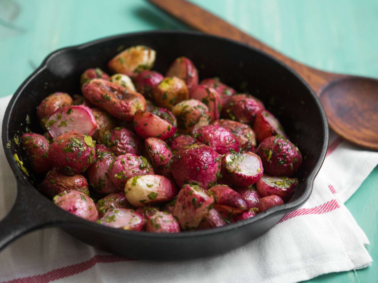 Cooked radishes garnished with herbs in a cast iron skillet placed on a cloth