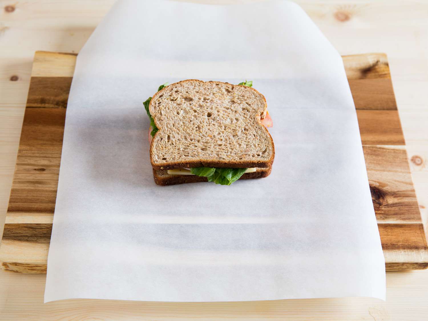 A sandwich placed on a sheet of parchment paper on top of a wood cutting board.