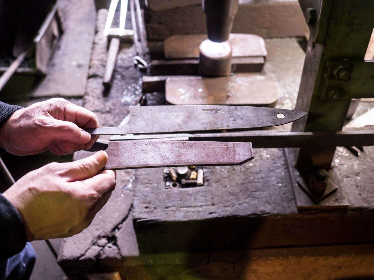 Two knife blanks are held up for inspection. One looks as though it snapped in half.