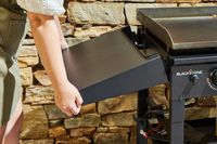 A person affixes a side table to the Blackstone 1554 Cooking 4 Burner Flat Top Gas Grill