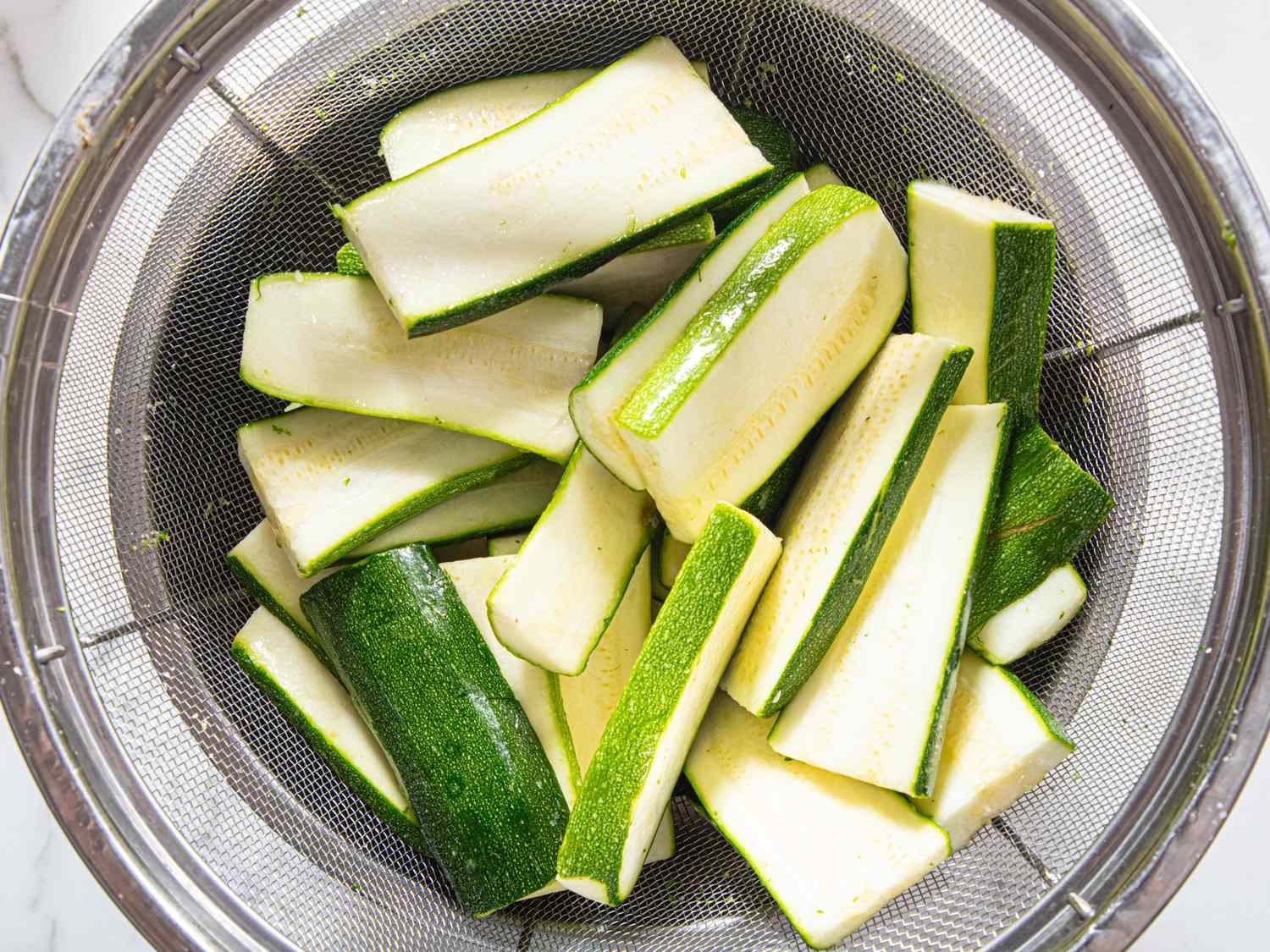 Sliced zucchini in a metal strainer