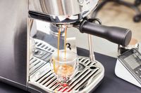 Closeup of Breville Bambino Plus Espresso Machine dispensing espresso coffee into a clear cup