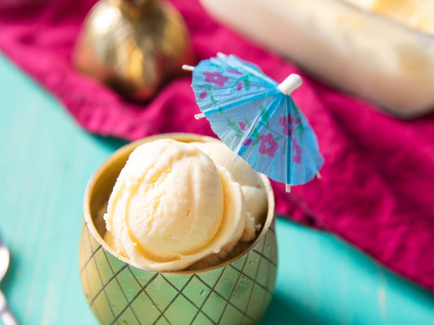 Close up of pineapple ice cream scoops in a golden glass, decorated with a paper umbrella.