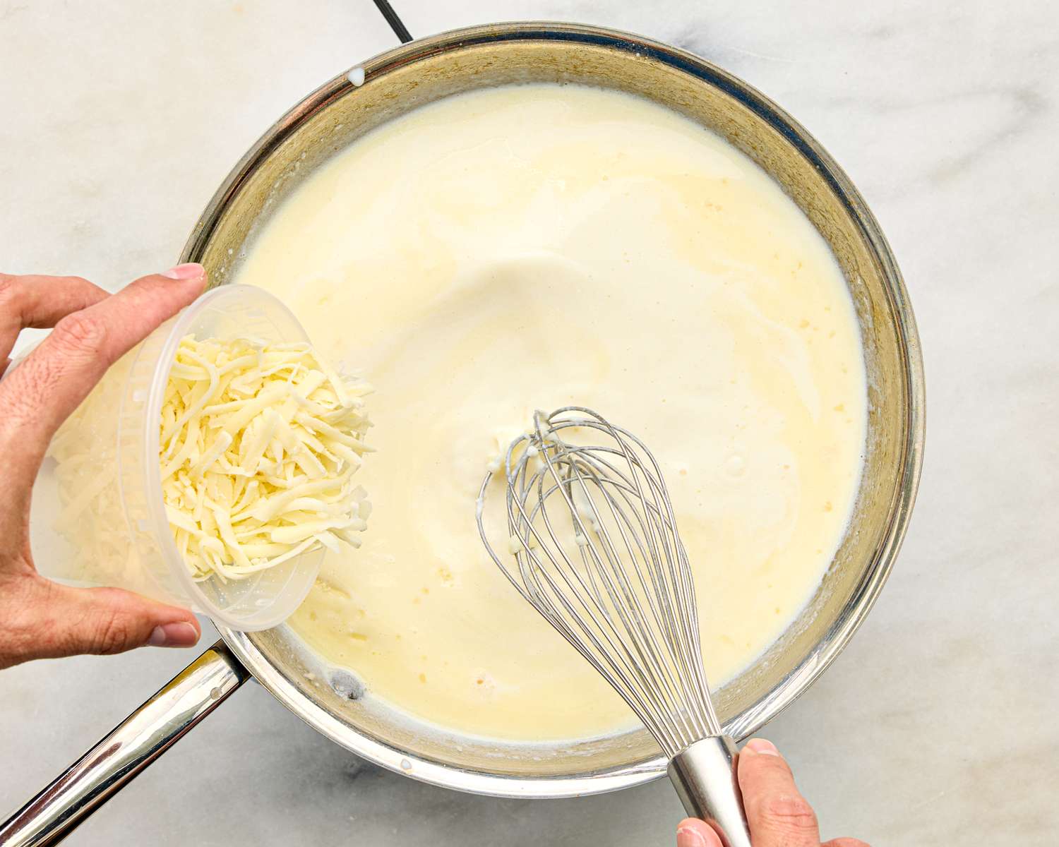 Preparing a creambased sauce in a pan with shredded cheese being added and whisking taking place