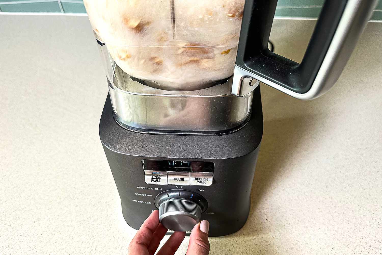 A person blending almonds and water in the Calphalon Auto Speed 68-Ounce Blender using the speed dial.