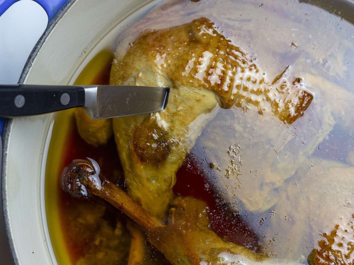Turkey in a large Dutch oven being pierced with a paring knife.