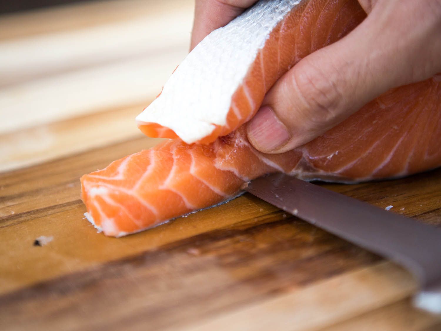 Using a knife to cut between the skin and a belly flap of a salmon steak.