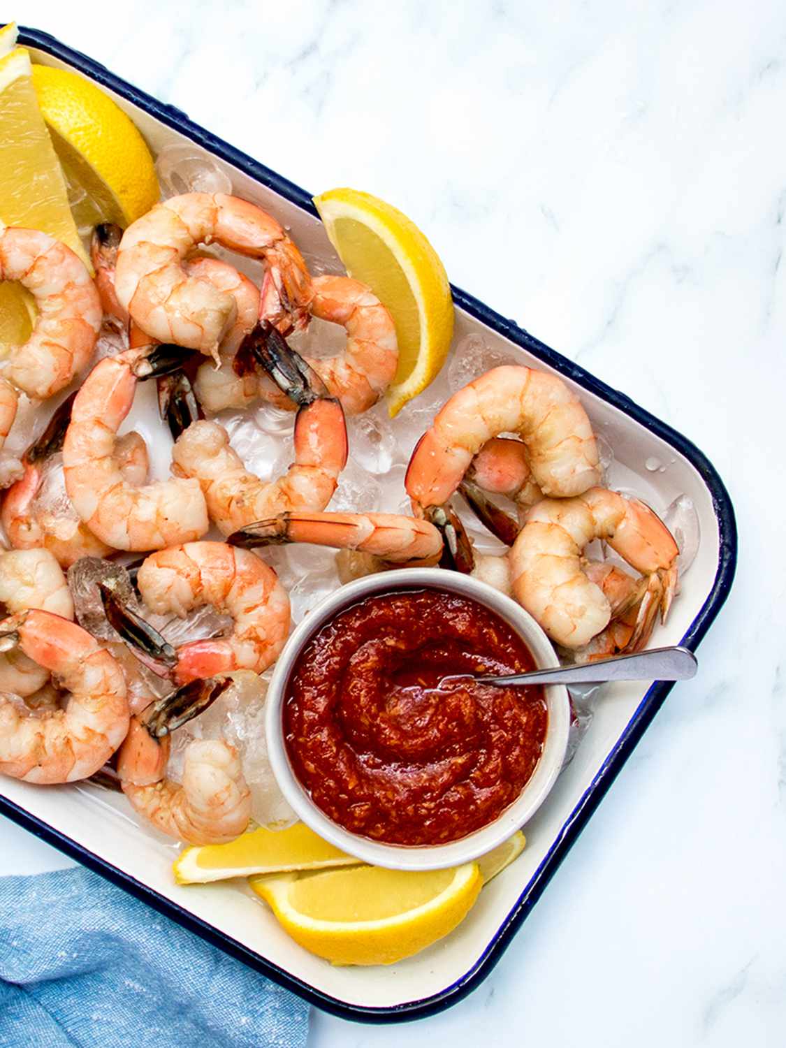 Shrimp, sliced lemons, and cocktail sauce on an enameled metal tray.