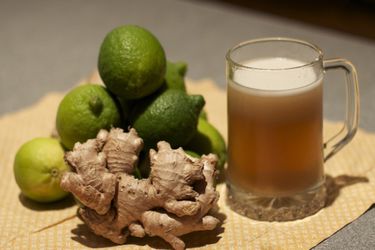 Stein of ginger beer displayed on straw mat with fresh ginger and limes