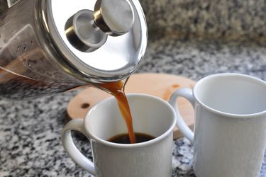 A French press pouring into two white coffee cups.
