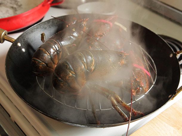 Whole lobsters steaming in a wok for Cantonese-style lobster with ginger and scallions.
